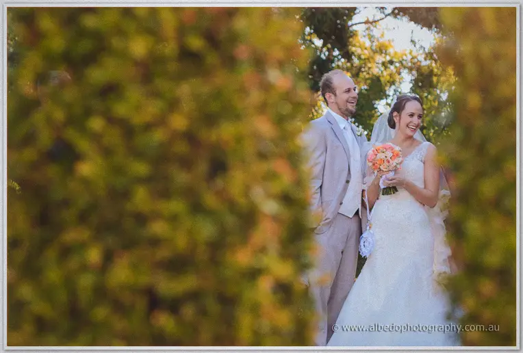 Katelyn and Matt smile through golden foliage in a warm Brookleigh garden portrait