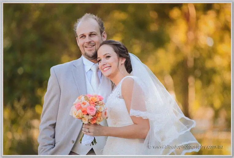 Katelyn leans on Matt's shoulder clutching her coral bouquet in golden afternoon light