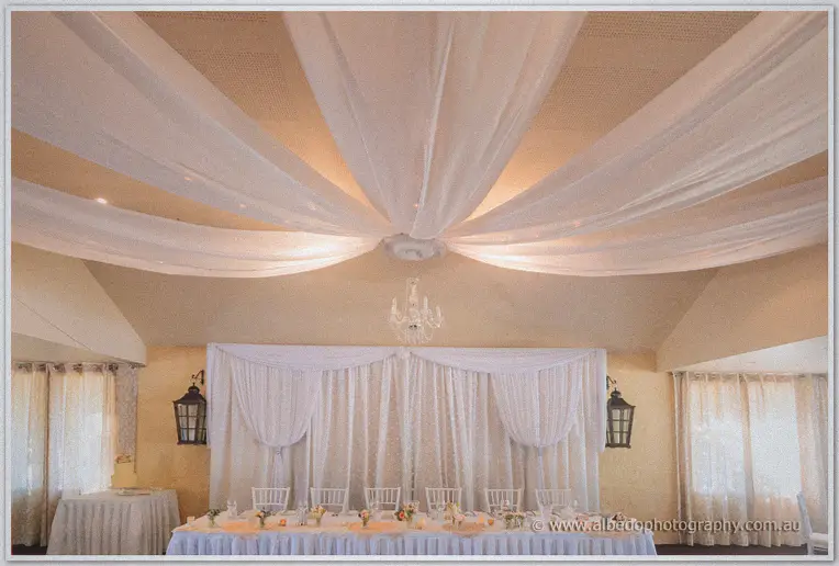 Reception room with white fabric swagged across the ceiling above the bridal table and cake