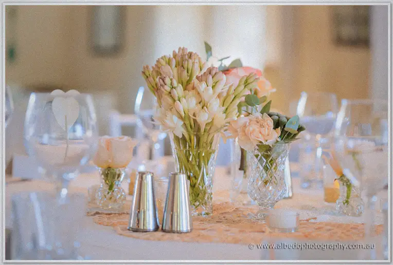 Crystal vases of tuberose and peach roses dot a lace-trimmed guest table in warm light