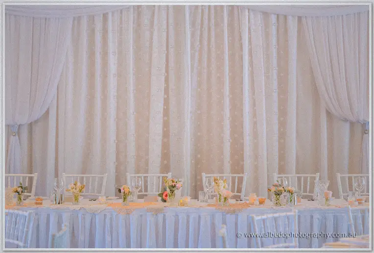 Bridal table dressed in white linen and peach posies against a draped lace curtain wall