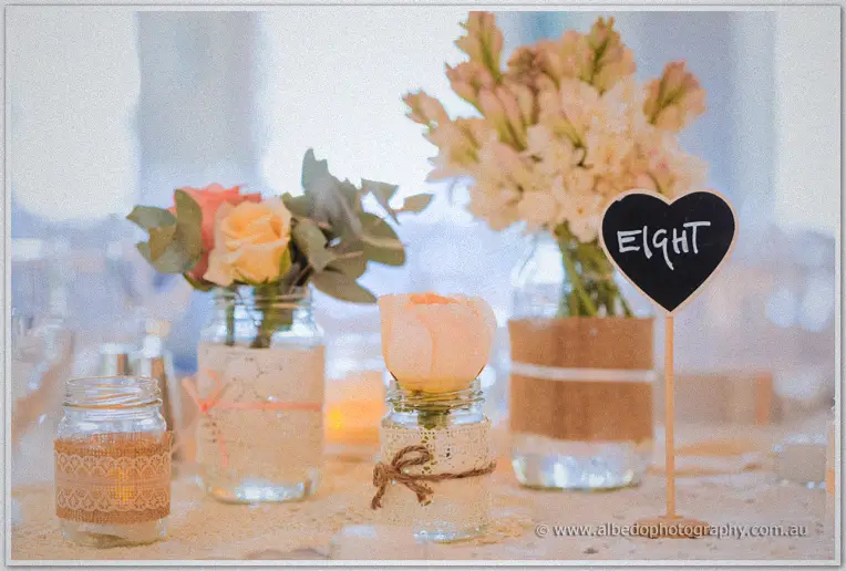 Lace-wrapped jars of roses and tuberose beside a heart sign marking table eight