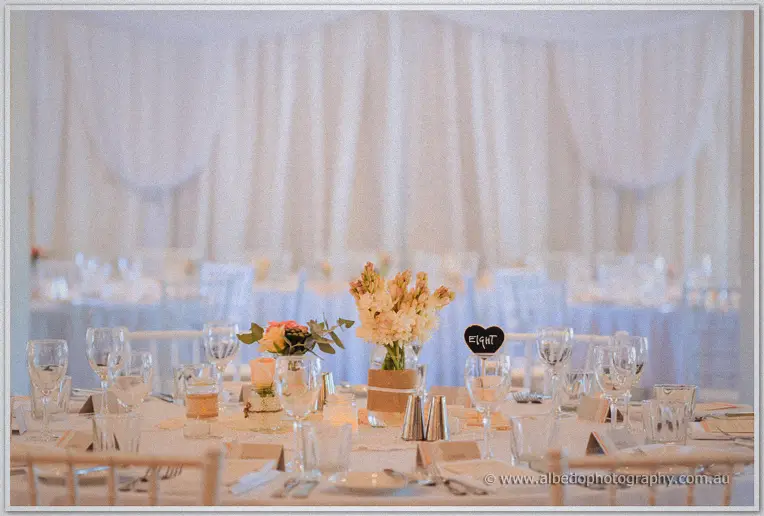 Guest table set with glassware and blooms before a curtained wall, heart chalkboard reading eight