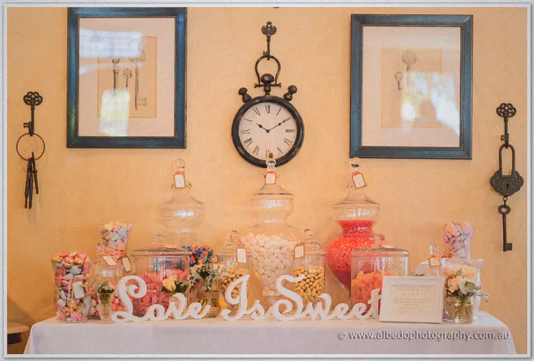Lolly buffet in glass jars beneath a vintage clock, white script reading love is sweet