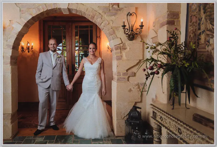 Katelyn and Matt holding hands beneath the stone archway of Brookleigh's homestead, candle sconces glowing