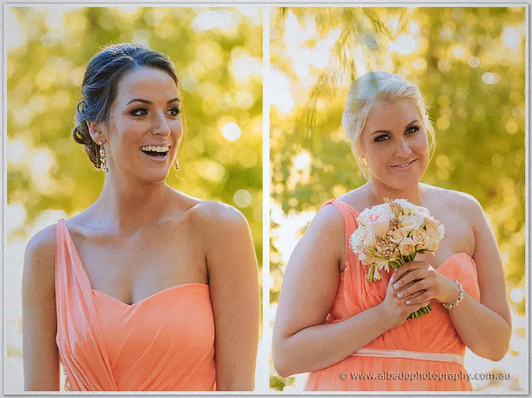 Two bridesmaids in coral gowns laughing in golden light, one clutching a peach and cream rose posy