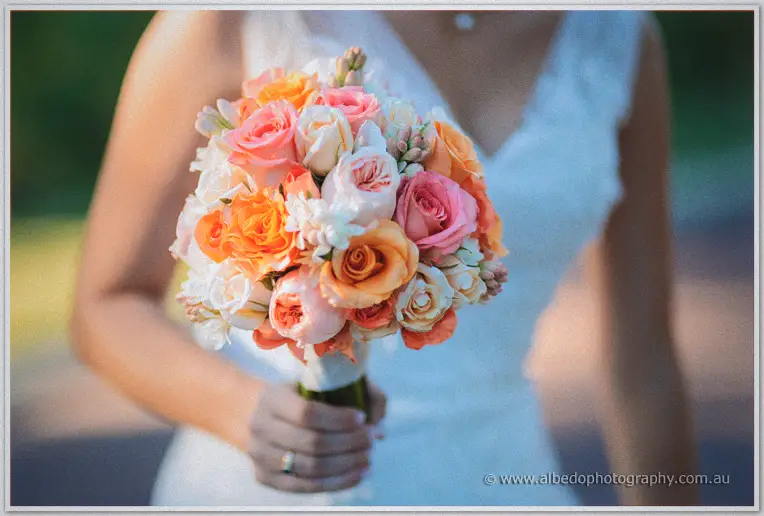 Close view of Katelyn's rounded bouquet of orange, coral and cream roses against her lace gown
