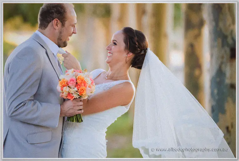 Katelyn tugging Matt's tie and laughing as her veil catches the afternoon light beside the gums