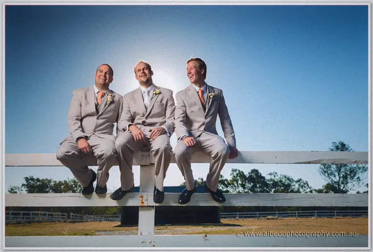 Matt and his groomsmen perched along a white paddock fence under a bright country sky