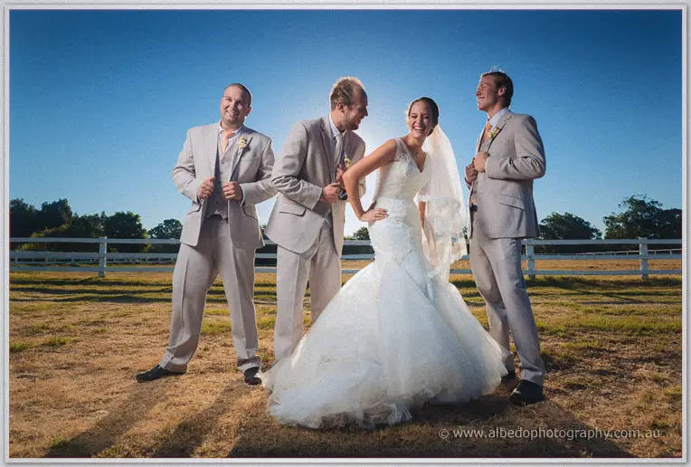 Katelyn laughing with Matt and the groomsmen as the guys adjust their jackets beside the fence
