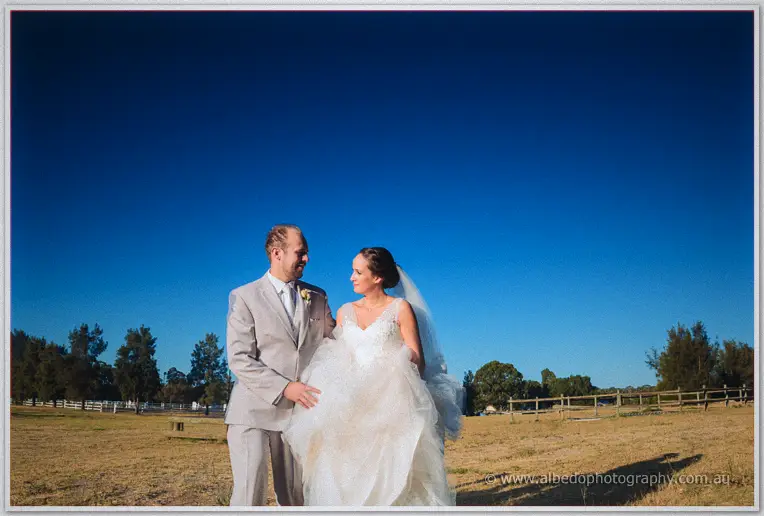 Katelyn and Matt grinning at each other in a dry paddock, her gathered skirt between them