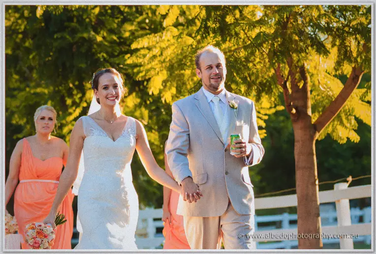 Katelyn and Matt walking hand in hand through sunlit trees, Matt carrying a green can