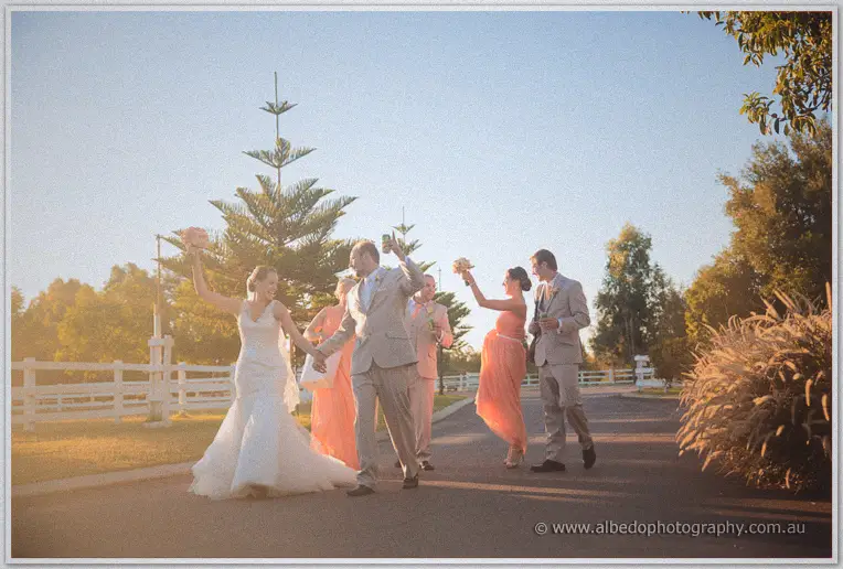 Bridal party celebrating on the driveway at sunset, Katelyn and a groomsman raising their arms