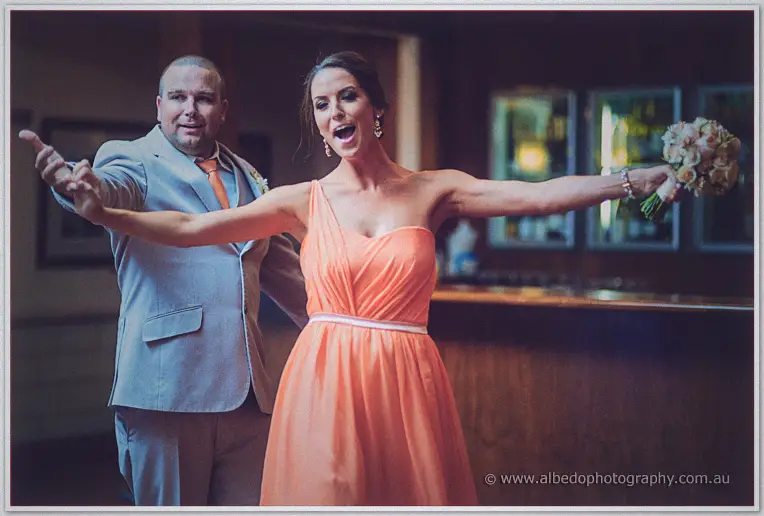 Bridesmaid in an orange gown striking a playful star pose with the MC beside the bar