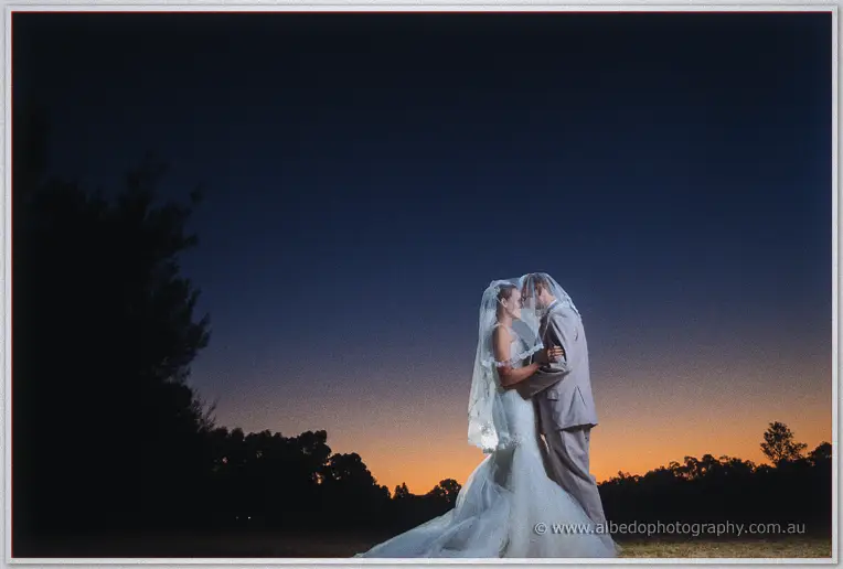 Katelyn and Matt kiss under her veil against an orange horizon as night falls at Brookleigh