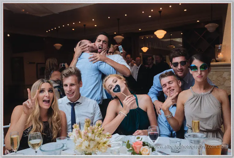 Wedding guests clown with props and peace signs at a lamp-lit reception table at Brookleigh