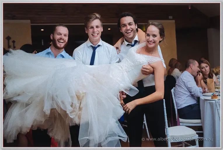 Laughing groomsmen hoist Katelyn sideways in her billowing gown at the reception