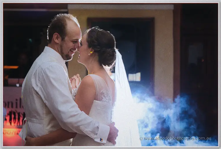 Katelyn and Matt smile nose to nose during their first dance amid drifting blue fog