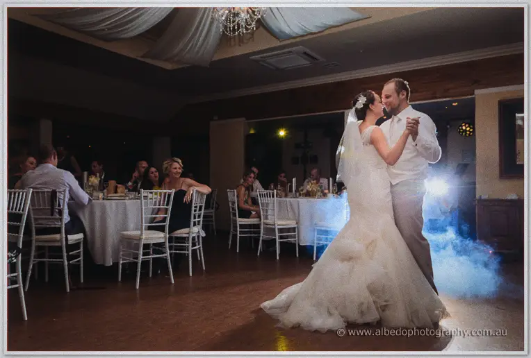 Wide view of Katelyn and Matt's first dance before seated guests under a draped chandelier