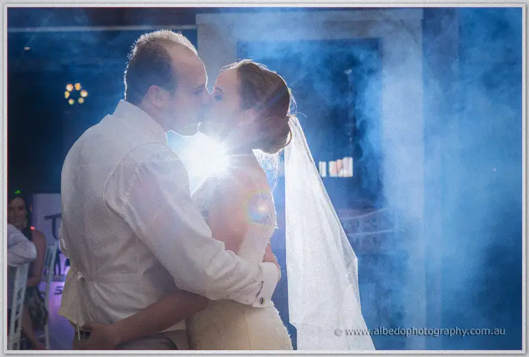 Katelyn and Matt kiss on the dance floor, backlit by a flare through hazy blue smoke