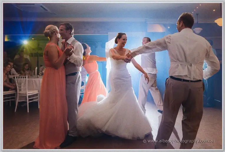 Katelyn dances with a groomsman among couples in coral dresses under party lights