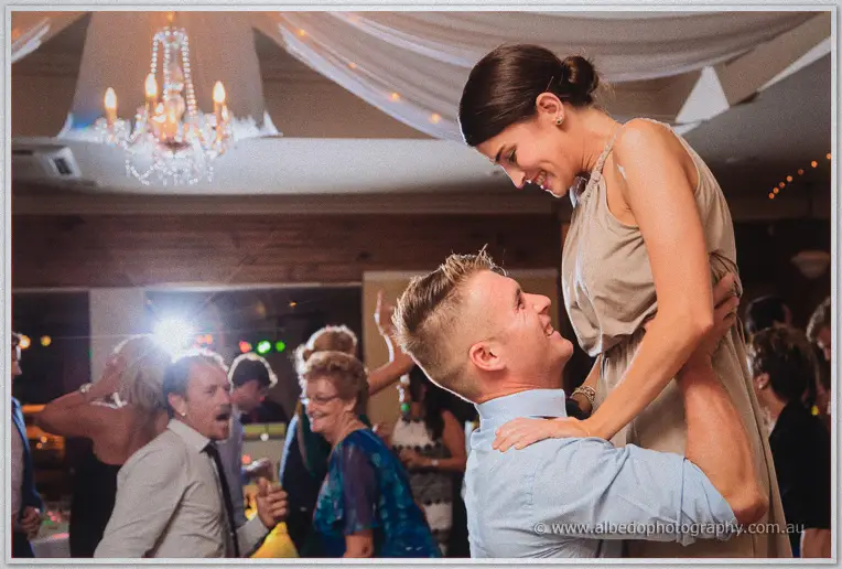 A groomsman lifts his partner high as they dance among the wedding crowd