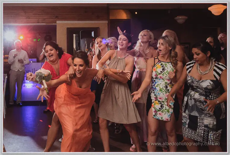A bridesmaid in coral lunges for the bouquet as guests crowd in behind her