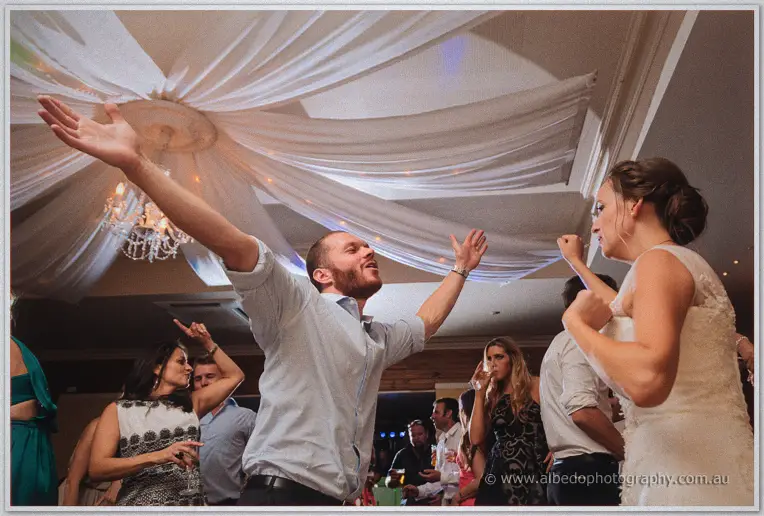 A bearded guest dances with arms flung wide beside Katelyn under the draped ceiling