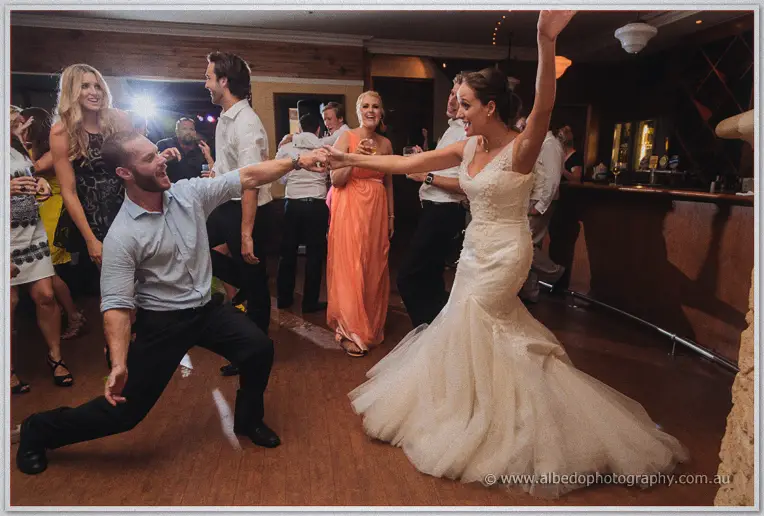 Katelyn pulls a lunging groomsman back up by the hand as guests laugh around them