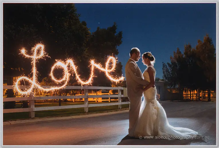 Sparkler light spells love in cursive beside Katelyn and Matt embracing on the night road