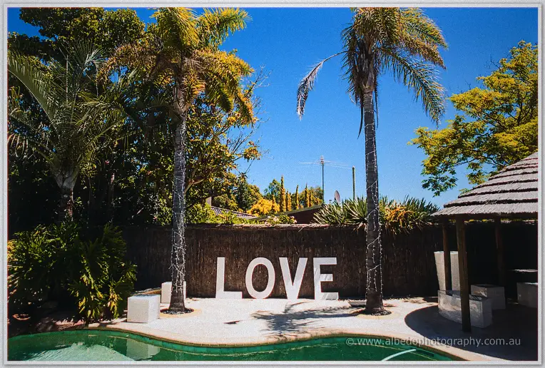 White LOVE letters standing between palm trees by the pool and thatched hut in a sunny backyard