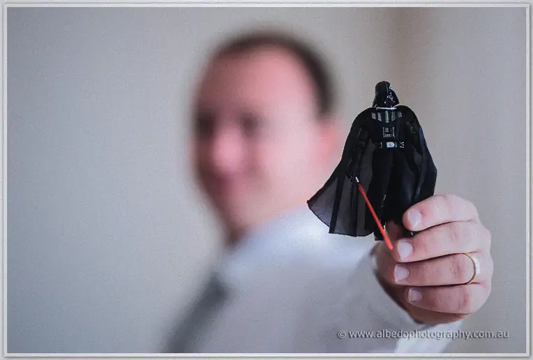 Smiling groomsman holding up a Darth Vader figurine in front of his blurred face