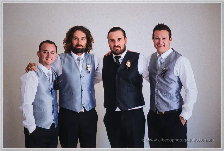 Troy and his three groomsmen posing in grey and black vests with toy figurine boutonnieres