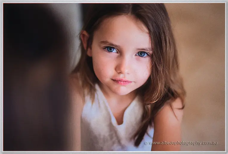 Portrait of the blue-eyed flower girl in a white lace top gazing softly at the camera
