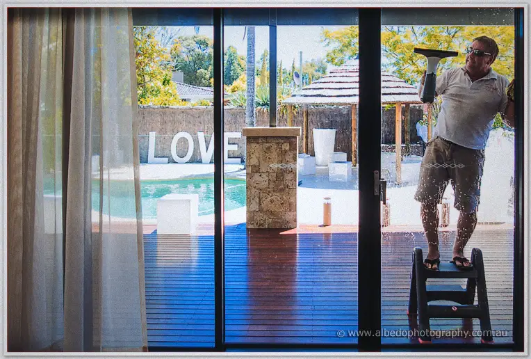 Window cleaner on a step ladder squeegees the poolside glass doors, LOVE letters in the reflection