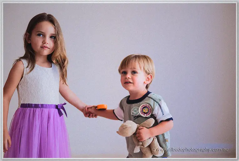 Flower girl leading her little brother by the hand, teddy bear tucked under his arm