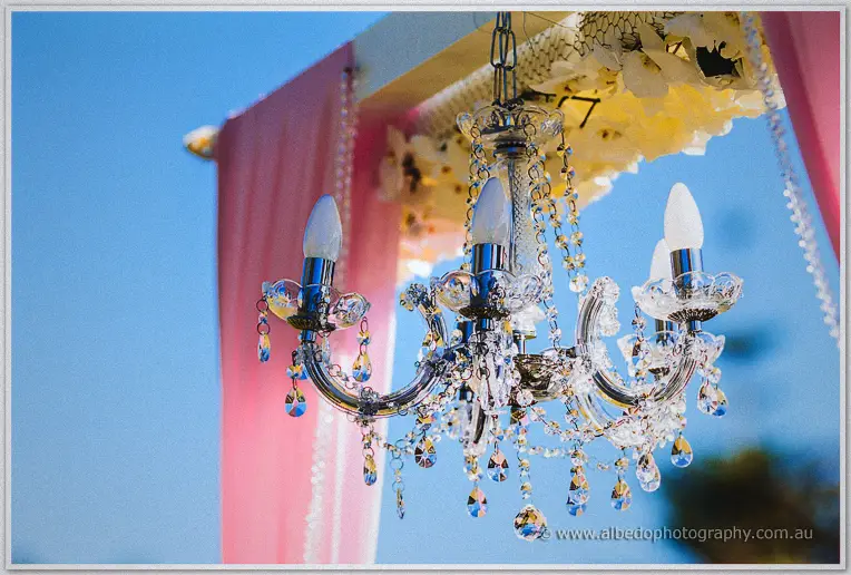 Crystal chandelier hanging against blue sky at the garden ceremony arbour draped in pink