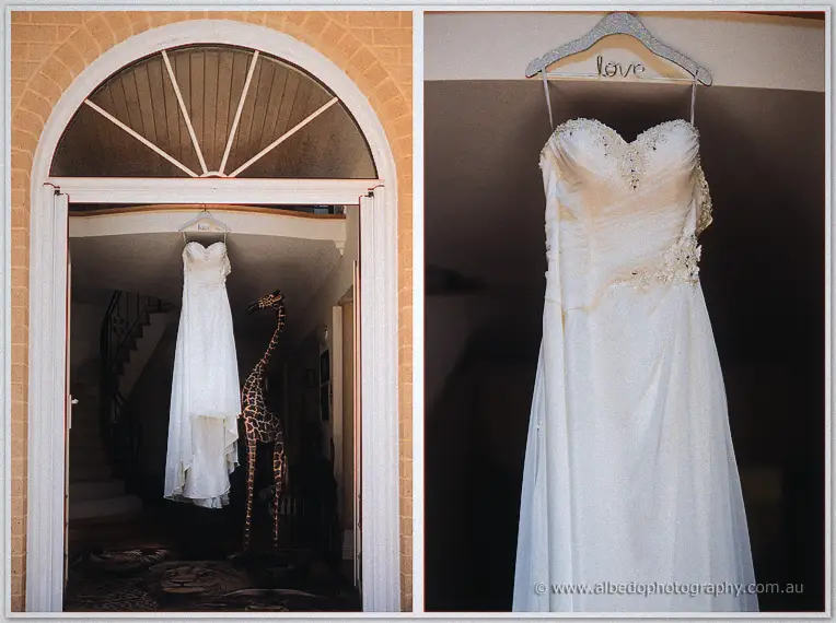 Bride's strapless gown hanging in the doorway beside a giraffe ornament and on a love hanger