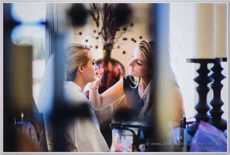 Teigan sits in a white robe while her makeup artist works, framed candidly through a doorway