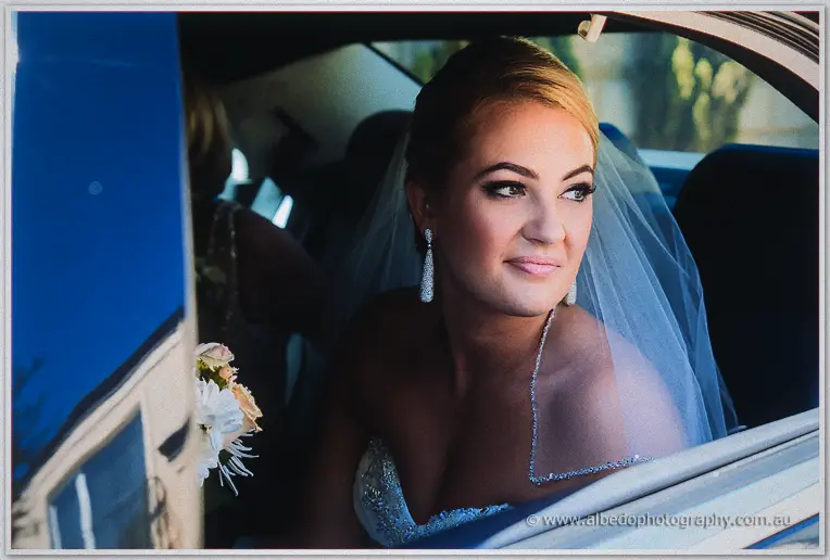 Veiled Teigan smiles from the limousine window with her pastel bouquet beside her