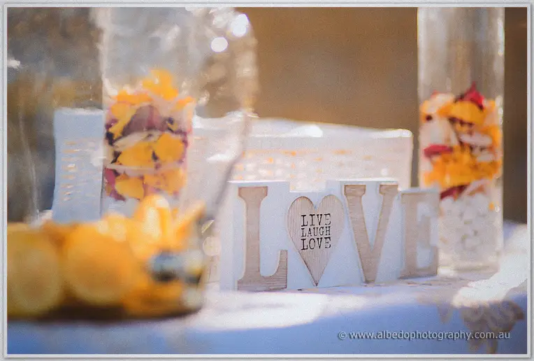 Wooden LOVE letters with a live laugh love heart sit among rose petals and petals filled jars