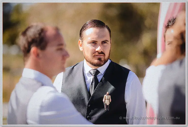 Groom Troy waits composed in black vest and tie with a small keepsake pinned to his chest