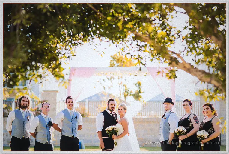 Bridal party stands beneath gum tree shade with the couple before the pink arbour