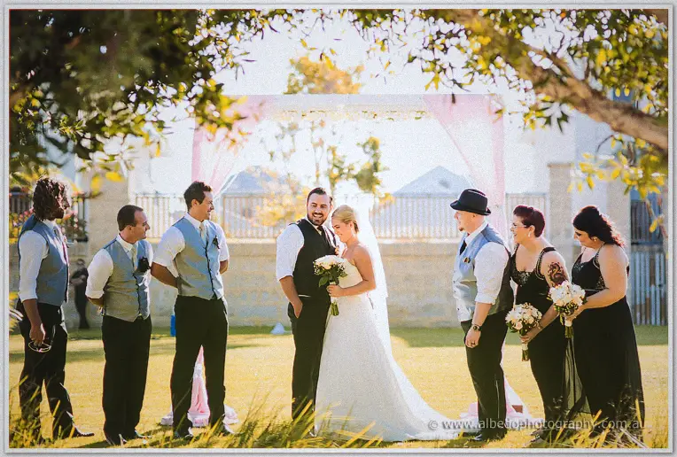 Troy and Teigan laugh with their bridal party in dappled light on the lawn