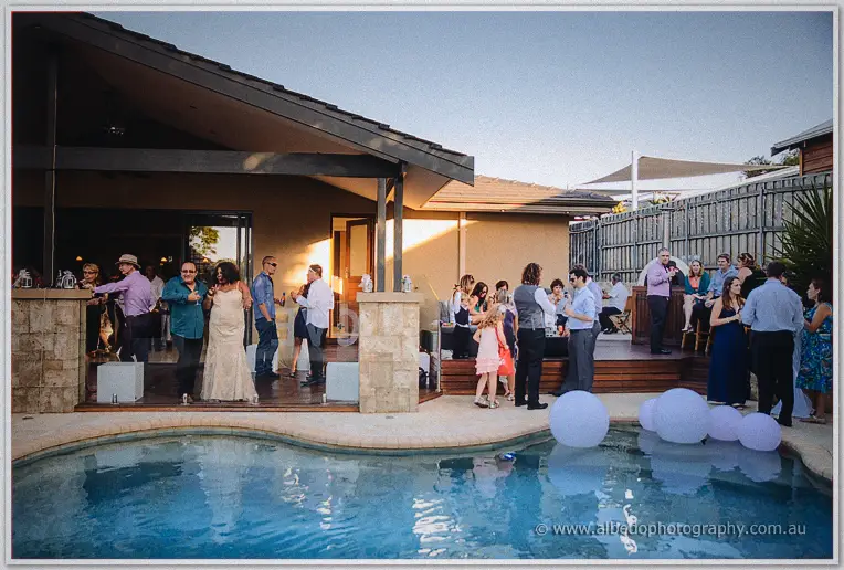 Guests mingle around the glowing pool among floating white balloons at dusk