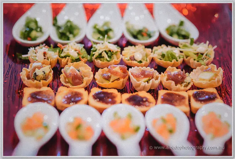 Rows of colorful canapes on ceramic spoons glow under red reception lighting