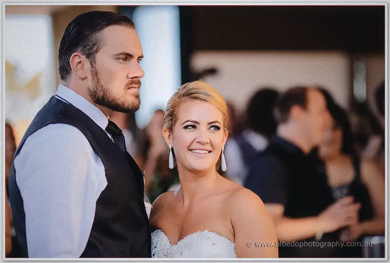 Teigan smiles over her shoulder as Troy watches the reception crowd behind them