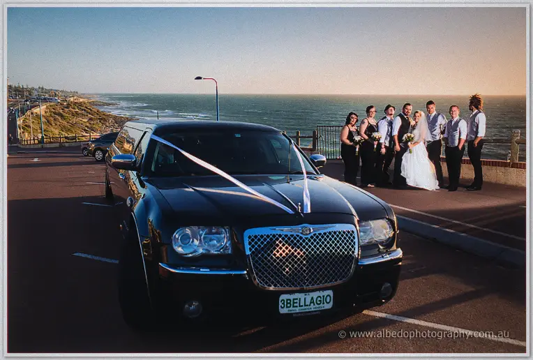 Ribbon-tied black limousine parked by the Hillarys oceanfront as the bridal party gathers at sunset