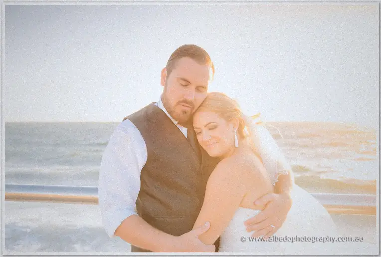 Teigan nestles into Troy's chest as sunset light glows over the ocean behind them