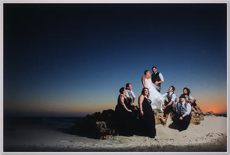 Full bridal party gathered on beach rocks against a vast evening sky and calm sea